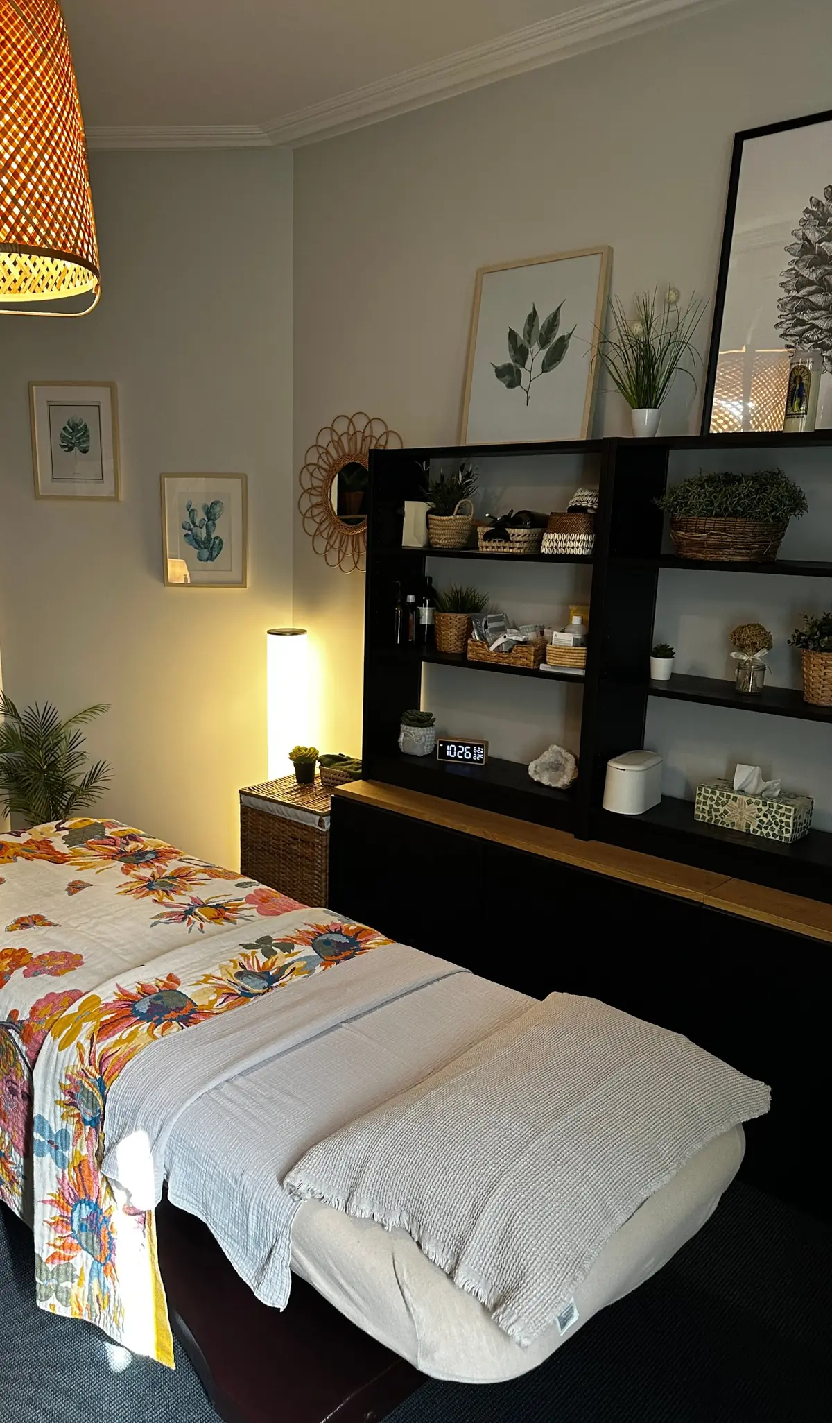 Cabine de l'atelier Pimp My Derm d'Asnières-sur-Seine : table de massage, plaid fleuri, suspension en osier, plantes et lumière douce