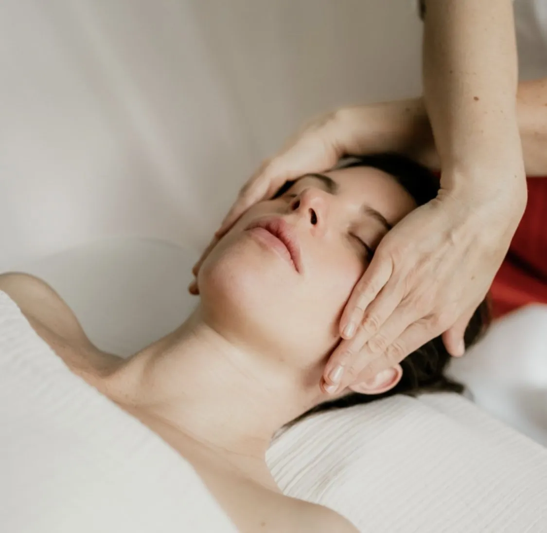 Mains de la facialiste posées sur les tempes et le visage d'une cliente