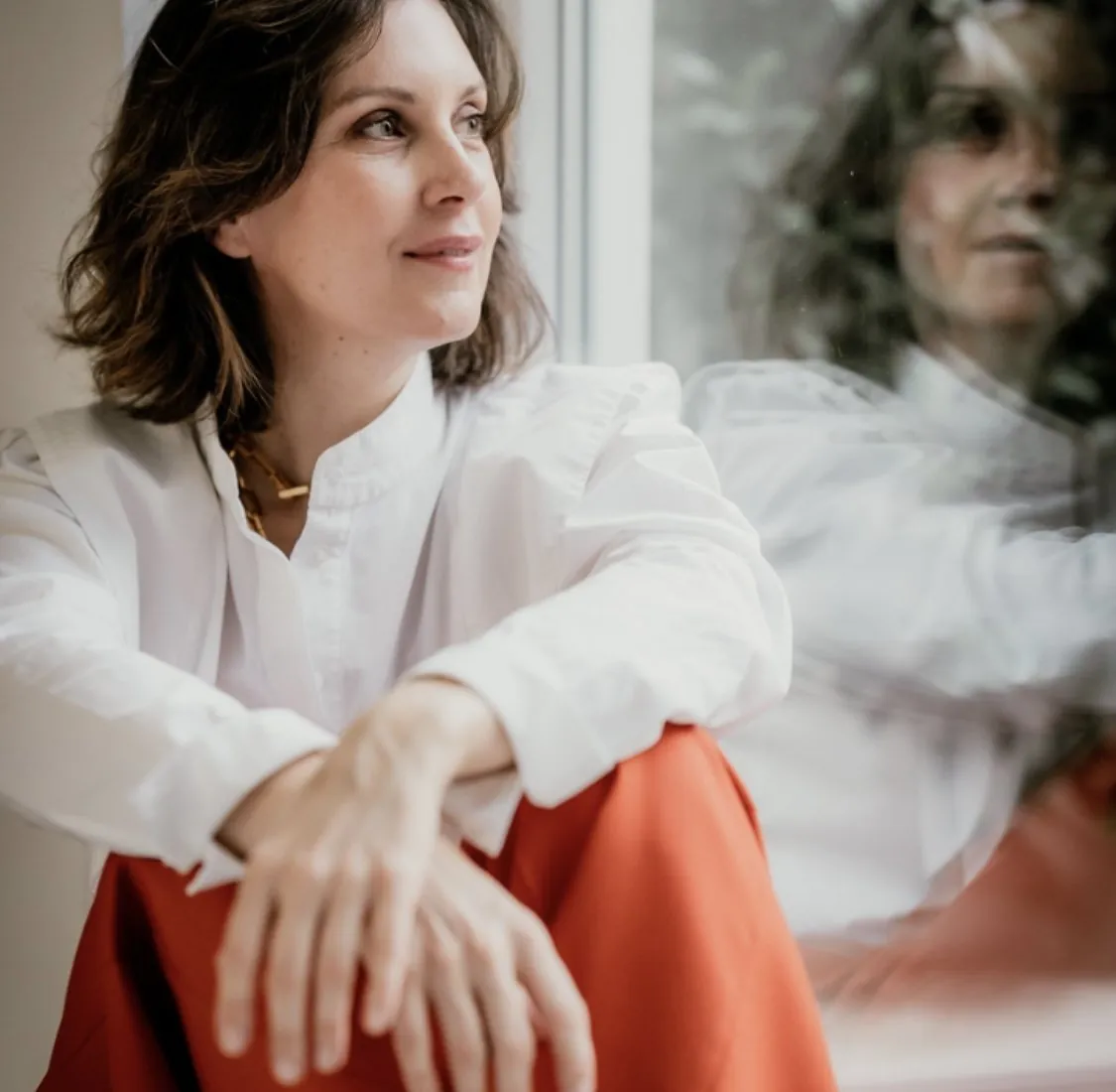 Virginie Tran, facialiste et fondatrice de Pimp My Derm, assise près d'une fenêtre en chemise blanche